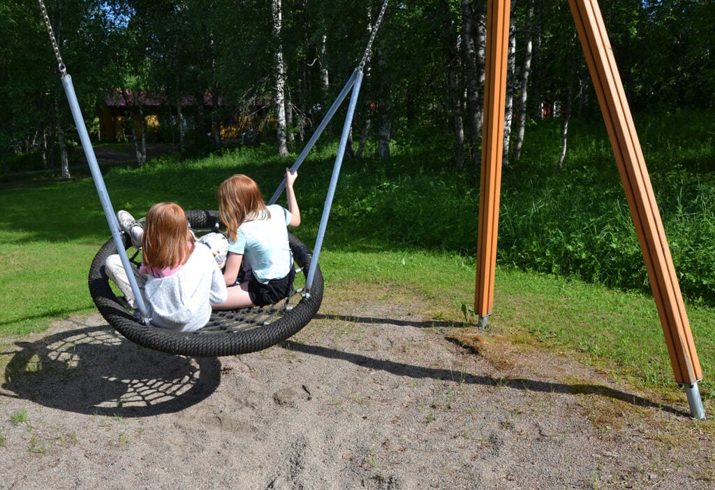 Kaksi lasta keinuu pyöreässä hämähäkkikeinussa.