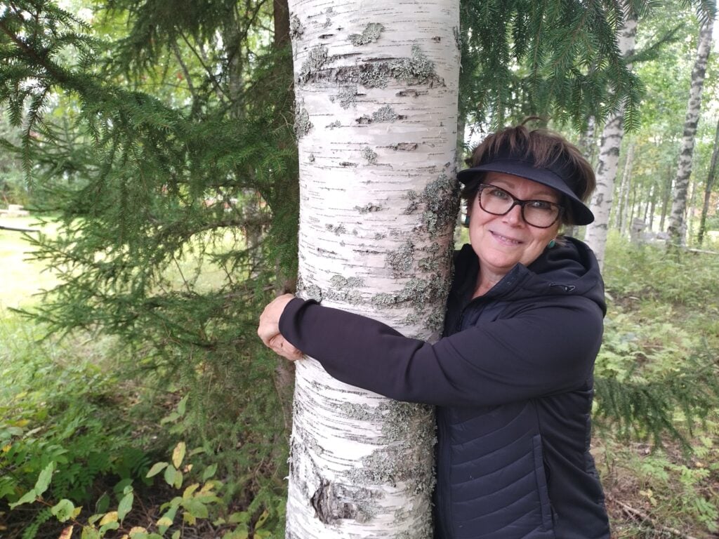 Nainen halaa koivunrunkoa metsässä.