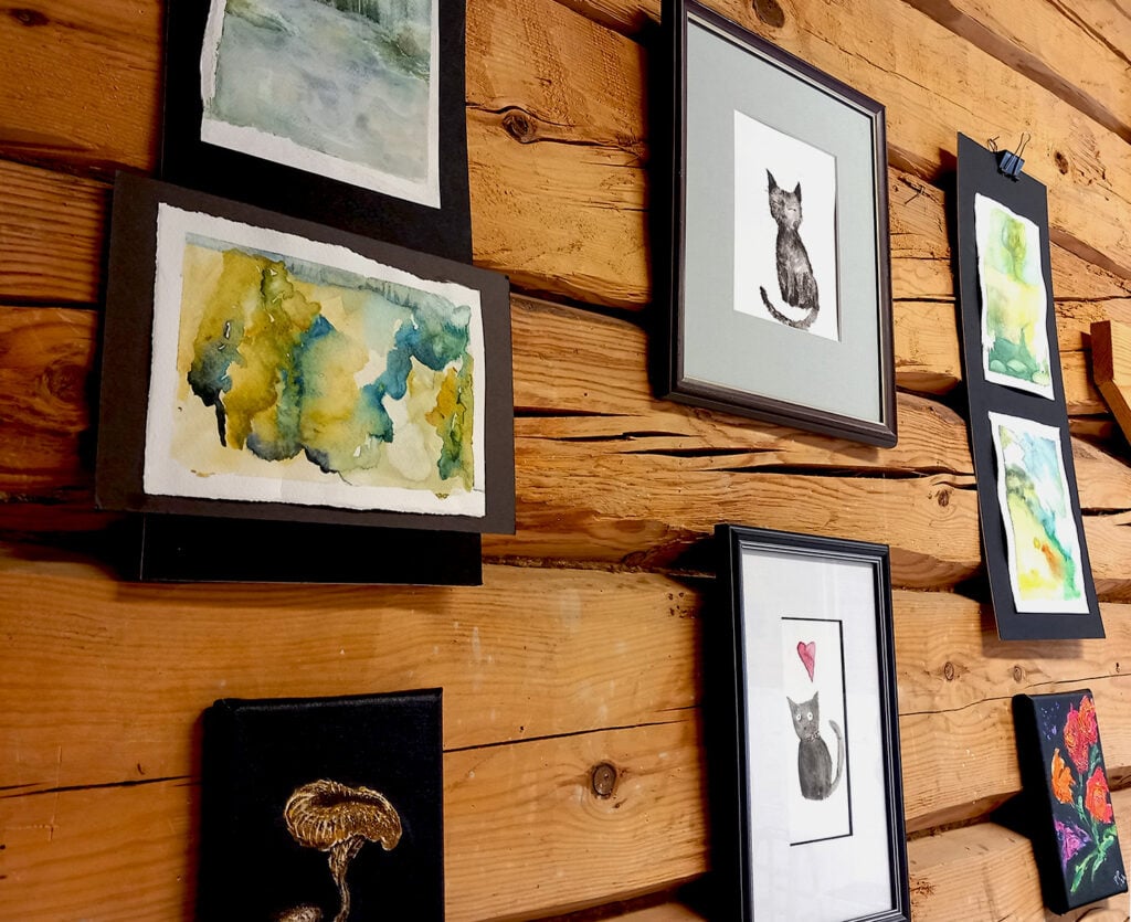 Hirsiseinä, johon ripustettu kuvataideopiskelijoiden kehystettyjä töitä.